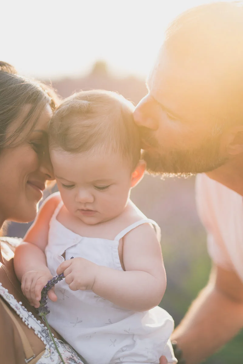 Sweet family pictures with parents kissing their baby during a photo session in lavender fields near valensole