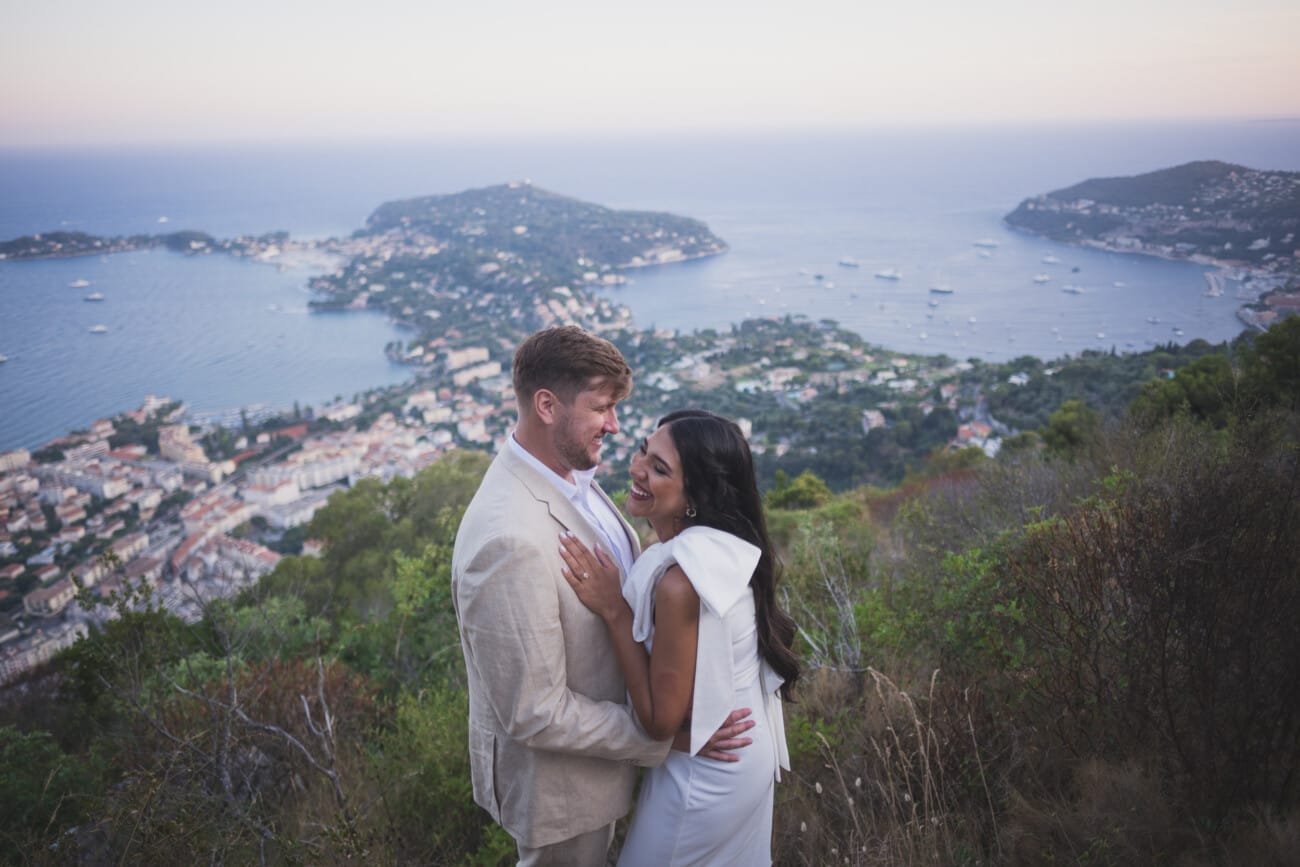 Above the Bay: An Intimate French Riviera Elopement on the Hillsides 28 Couple laughing with wedding outfits and French Riviera bay of Villefranche-sur-Mer in the far back