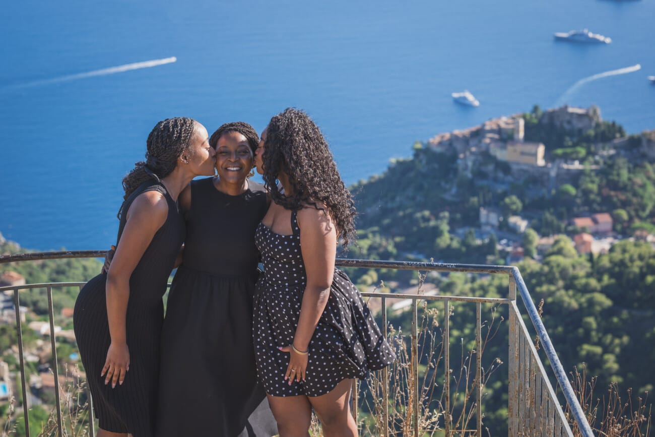 The Ultimate Girls’ Trip: A Mother and Daughters’ Legacy Session on the French Riviera 4 Mother embracing her two adult daughters with the dramatic coastline of the South of France in the background.